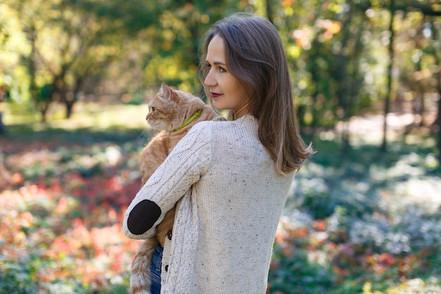 Retrato de uma mulher segurando um grande gato fofo vermelho na natureza, garota feliz e lindo gato fofo ao ar livre