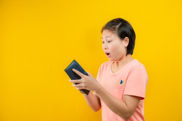 Retrato de uma mulher segurando uma carteira surpresa que não há dinheiro em sua bolsa contra uma poupança de background.concept amarelo.