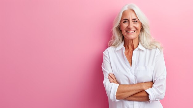 Retrato de uma mulher sênior feliz com os braços cruzados em fundo rosa