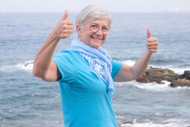 Retrato de uma mulher sênior feliz e atraente em camiseta azul e cachecol desfrutando de férias ao ar livre no mar