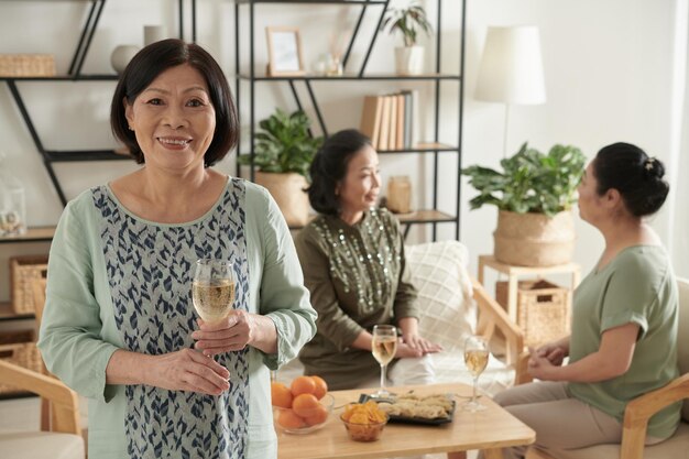 Retrato de uma mulher sênior positiva com copo de vinho seus amigos falando em segundo plano