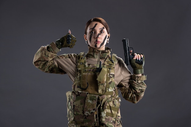 Retrato de uma mulher soldado camuflada com arma de parede escura