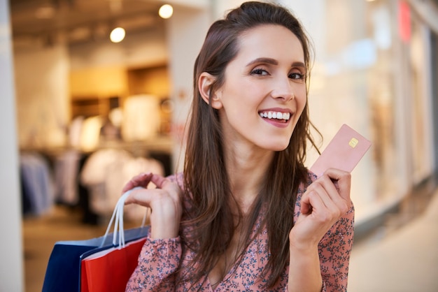 Retrato de uma mulher sorridente com cartão de crédito e sacolas de compras