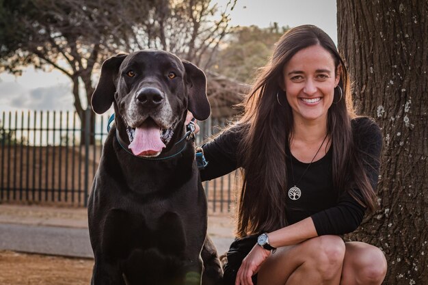 Foto retrato de uma mulher sorridente com um cão sentado contra uma árvore