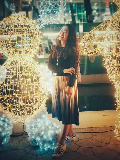 Foto retrato de uma mulher sorridente de pé junto a decorações iluminadas à noite