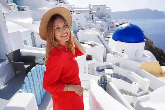Retrato de uma mulher sorridente de vestido vermelho se vira e sorri para a câmera quando desce os degraus na vila de Oia Grécia Europa