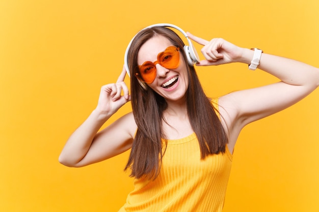 Retrato de uma mulher sorridente em óculos laranja, ouvindo música em fones de ouvido copie o espaço isolado em fundo amarelo. Emoções sinceras de pessoas, descanso de estilo de vida, relaxe o conceito de bom humor. Área de publicidade.