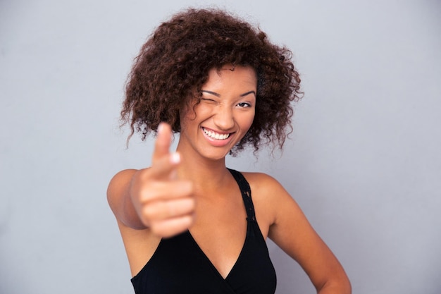 Retrato de uma mulher sorridente mostrando gesto de arma na frente na parede cinza
