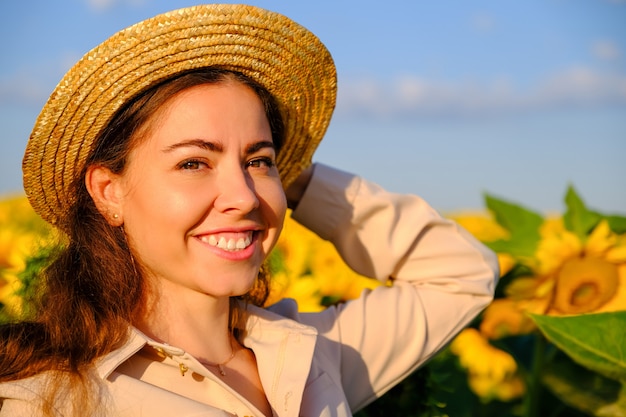 Retrato de uma mulher sorridente no chapéu de palha no campo de girassol florescendo