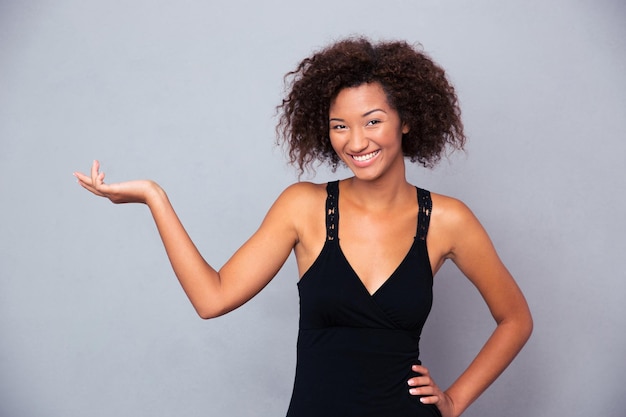 Retrato de uma mulher sorridente segurando copyspace na palma da mão sobre uma parede cinza e olhando para a frente