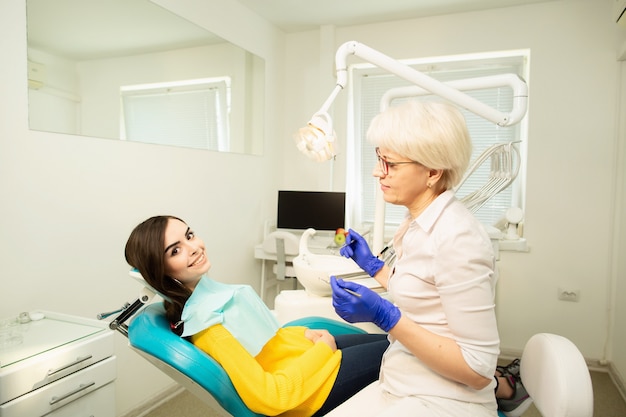 Retrato de uma mulher sorridente, sentado na cadeira odontológica com médico no consultório odontológico