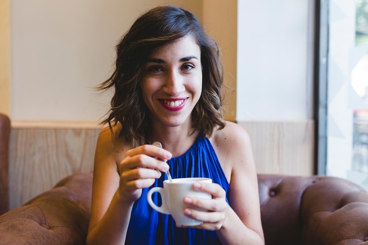 Foto retrato de uma mulher sorridente tomando café enquanto está sentada em um café