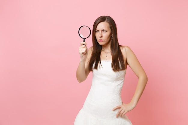 Retrato de uma mulher suspeita em um vestido branco examinando olhando através de uma lupa