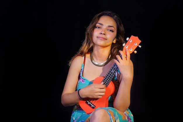 Retrato de uma mulher tocando o ukulele isolar em fundo preto. Livre do espaço da cópia