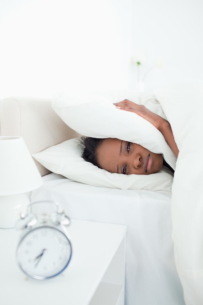 Retrato de uma mulher triste cobrindo as orelhas enquanto o despertador está tocando