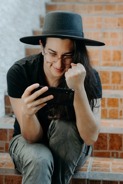 Retrato de uma mulher usando o telefone celular, usando óculos um chapéu preto.