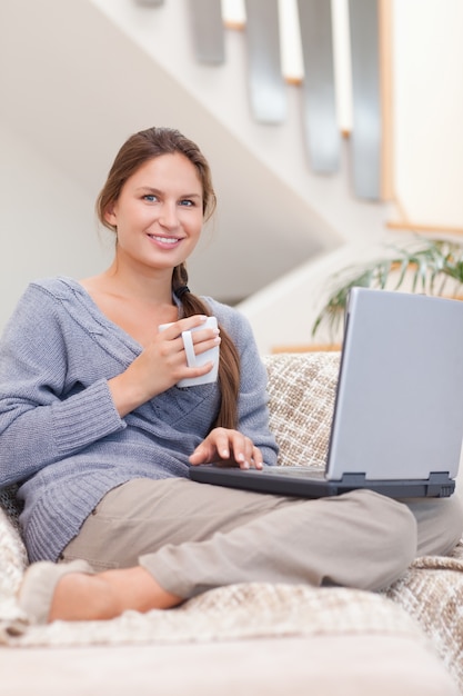 Retrato de uma mulher usando um laptop enquanto toma um café