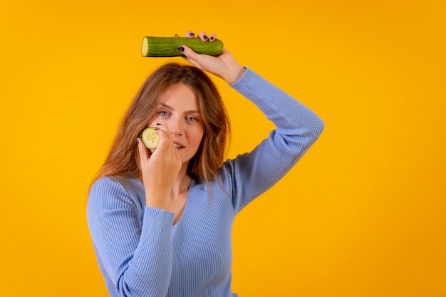 Retrato de uma mulher vegana segurando um pepino cortado em uma vida vegetariana de fundo amarelo