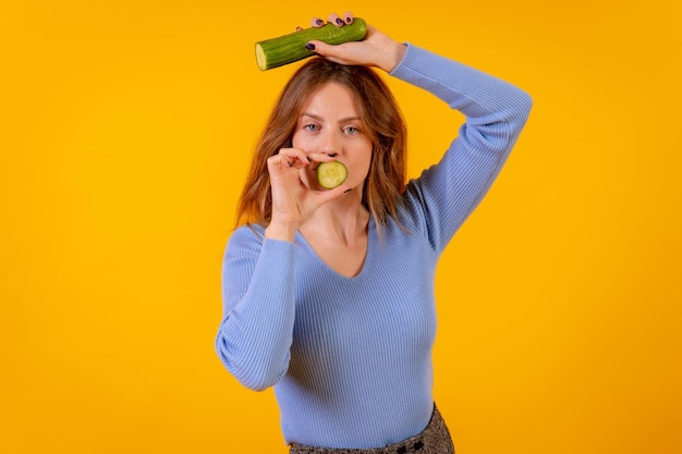 Retrato de uma mulher vegana segurando um pepino em uma vida vegetariana de fundo amarelo