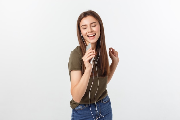 Retrato de uma música de escuta da mulher bonito alegre nos fones de ouvido e na dança isolados em um branco.