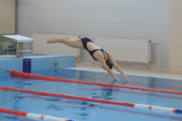 Retrato de uma nadadora, que salta e mergulha na piscina interior desportiva. Mulher desportiva.