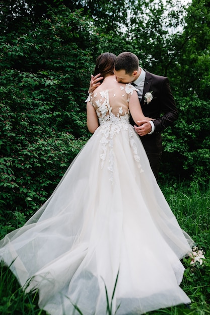 Retrato de uma noiva atraente de volta que abraça e beijando o noivo. Cerimônia de casamento. Recém-casados se casando na floresta.