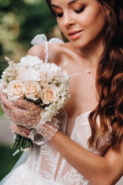 Retrato de uma noiva elegante em um vestido branco com um buquê na natureza em um parque natural. Modelo em um vestido de noiva e luvas e com um buquê.