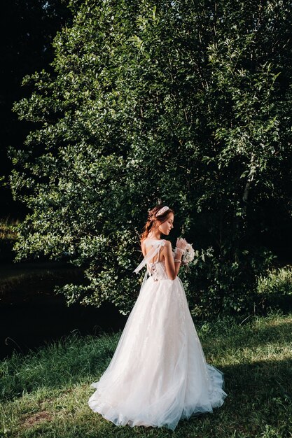 Retrato de uma noiva elegante em um vestido branco com um buquê na natureza em um parque natural. Modelo em um vestido de noiva e luvas e com um buquê.