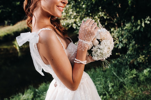 Retrato de uma noiva elegante em um vestido branco com um buquê na natureza em um parque natural. Modelo em um vestido de noiva e luvas e com um buquê.