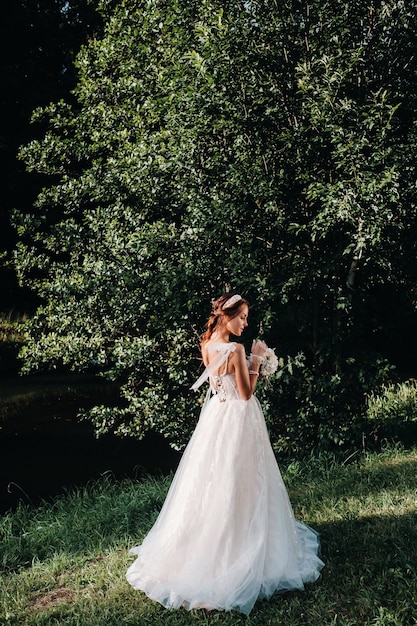 Retrato de uma noiva elegante em um vestido branco com um buquê na natureza em um parque natural