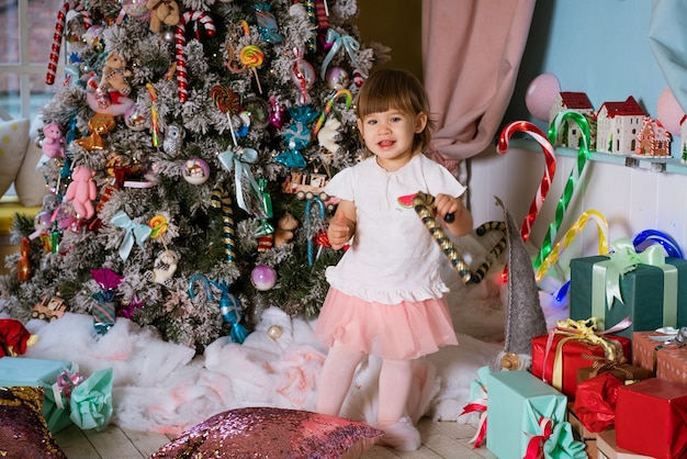 Retrato de uma pequena menina loira brincando perto da árvore de Natal, a criança está vestindo um ts branco.