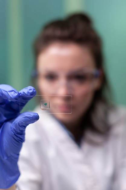 Retrato de uma pesquisadora botânica segurando um copo médico com uma amostra de folha verde