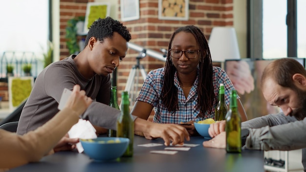 Retrato de uma pessoa alegre jogando jogos de tabuleiro com amigos, se divertindo com a estratégia e a competição de cartas. Jovens curtindo a jogabilidade na mesa, tomando cerveja e lanches.