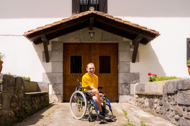 Retrato de uma pessoa com deficiência vestida de amarelo em cadeira de rodas na entrada de sua casa sorrindo