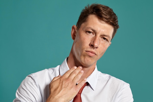 Retrato de uma pessoa morena imponente com olhos castanhos, vestindo uma camisa branca clássica e gravata vermelha. Ele está agindo como farto de posar em um estúdio contra um fundo azul. Conceito de gesticulação e s