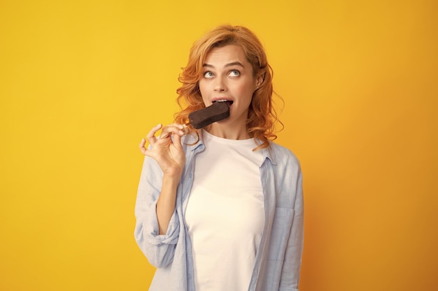 Retrato de uma ruiva com sorvete de chocolate em fundo amarelo Mulher alegre encaracolada comendo