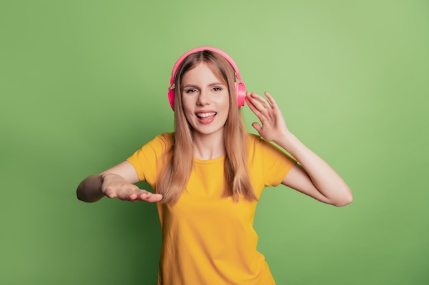 Retrato de uma senhora alegre e divertida dj ouvir música tocar faixa usar fones de ouvido com camiseta amarela sobre fundo verde