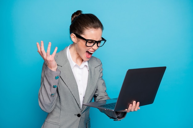 Retrato de uma senhora atraente, louca e irritada, furiosa, segurando o laptop de mão chorando isolado sobre um fundo de cor azul brilhante