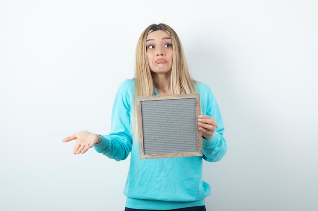 Retrato de uma senhora bonita segurando uma moldura contra uma parede branca