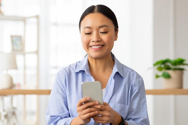 Retrato de uma senhora chinesa feliz usando um telefone celular em casa