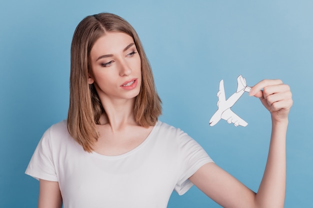 Retrato de uma senhora deslumbrante e tentadora segurando um avião de papel branco em um vôo sobre fundo azul