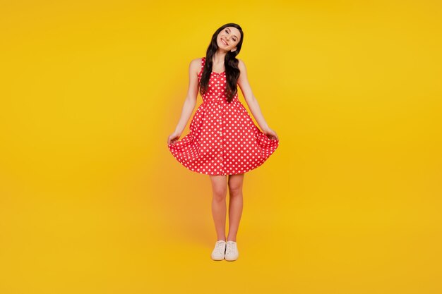 Retrato de uma senhora encantadora feminina posando com um vestido vermelho pontilhado em fundo amarelo