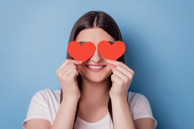 Retrato de uma senhora engraçada adorável segurando uma capa de cartão postal em forma de coração vermelho fechando os olhos sobre um fundo azul