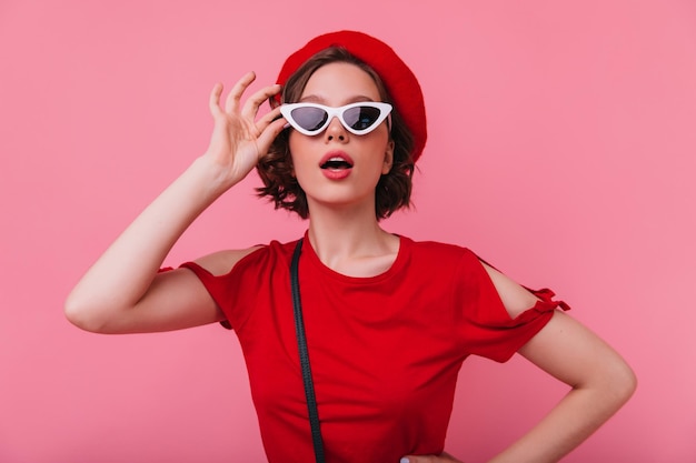 Retrato de uma senhora francesa inspirada posando em elegantes óculos de sol brancos foto de estúdio de elegante modelo feminino europeu com cabelo escuro curto