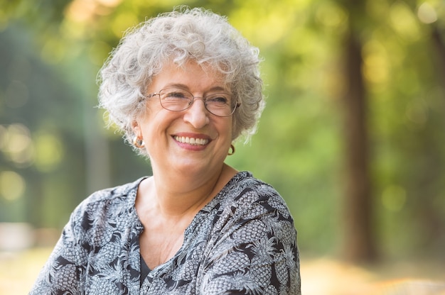 Foto retrato de uma senhora idosa sorridente com óculos no parque