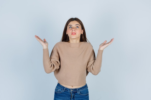 Retrato de uma senhora maravilhosa com as palmas das mãos para o lado enquanto olha para cima em um suéter, jeans e vista frontal focada