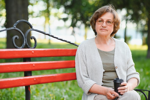 Retrato de uma senhora pacífica e envelhecida sentada no banco segura café