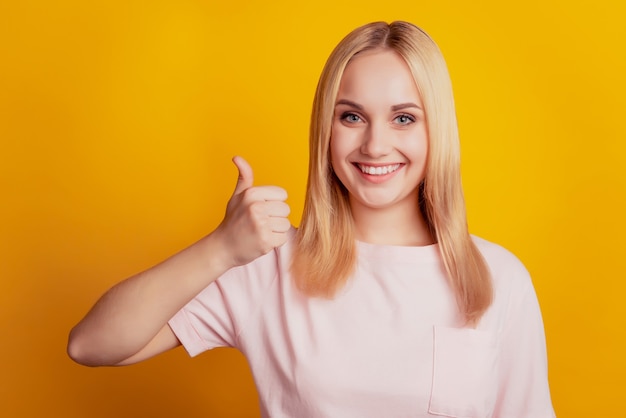 Retrato de uma senhora promotora confiável, sorriso dentuço, levantando o polegar sobre fundo amarelo