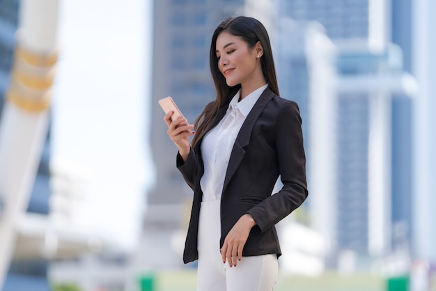 Retrato de uma sorridente mulher de negócios segurando um telefone em frente a edifícios de escritórios modernos