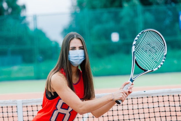 Retrato de uma tenista segurando uma raquete do lado de fora com máscara protetora